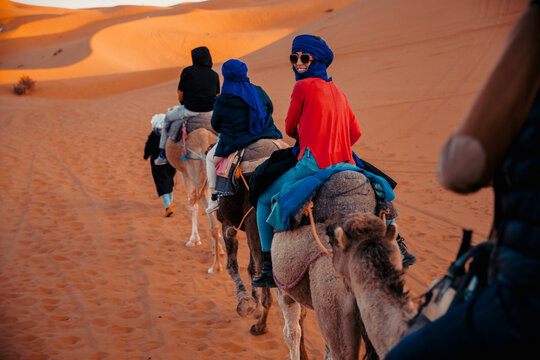 Woman with blue djellaba riding a camel among the dunes of the Sahara desert
