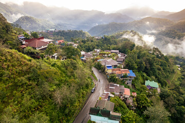 Fototapeta na wymiar Aerial view of a mountainous town with lush greenery and typical hillside houses, enveloped in morning mist. At the town of Banaue, in the province of Ifugao, Philippines.