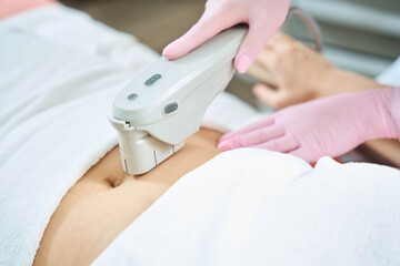 Cropped image of female beautician doing laser depilation of woman belly - obrazy, fototapety, plakaty