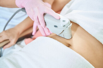 Beautician doing laser depilation of woman belly in blurred beauty salon