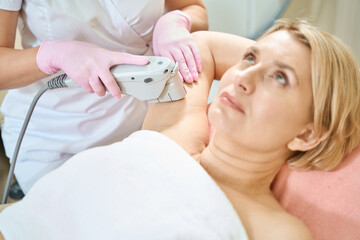 Cropped female cosmetologist doing laser depilation of hand of caucasian woman