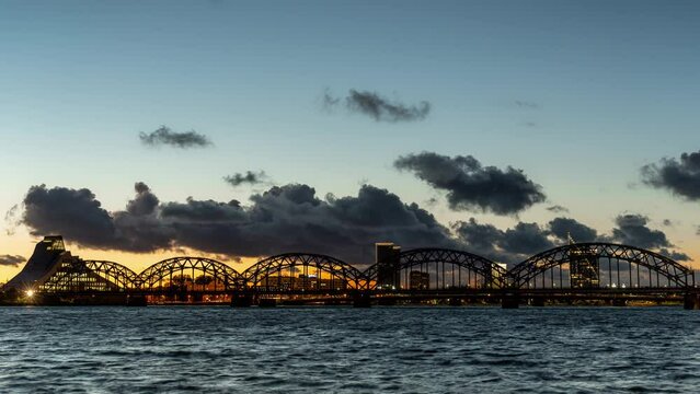Panoramic sunset timelapse of Riga skyline and steel railway bridge over Daugava river, scenic clouds in the background