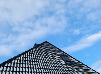 Open roof window in velux style with black roof tiles.