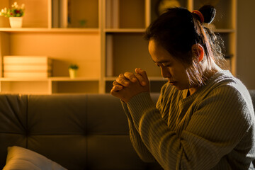 Christian religious woman praying at night sitting on couch in living dark room at home. Human person hands worship, Concept of praying to God. Female prayer with holy bible. Lady thanksgiving night