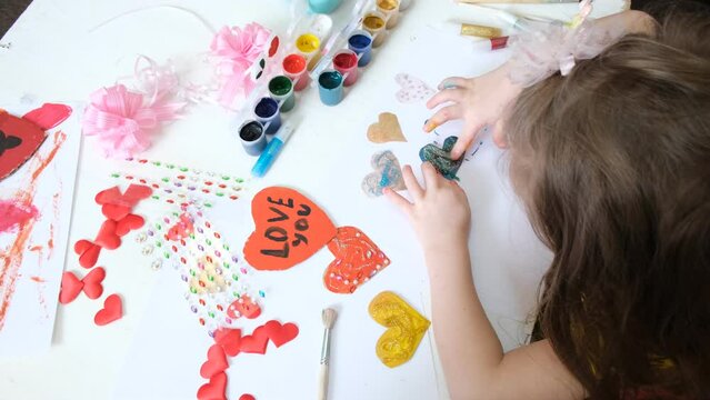 Child making homemade greeting card. A little girl paints hearts and funny pet as a gift for Mother’s Day or VAlentines day . Traditional play concept. Arts and crafts concept.