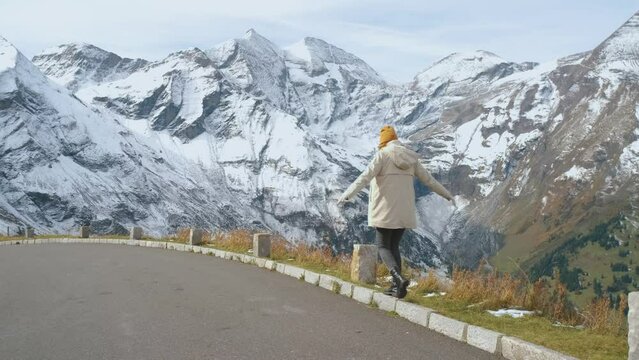 Beautiful girl traveler walks along Majestic Grossglockner Mountain Road in Austria, snow covered sharp peaks of the alpine mountains on background. Incredibly beautiful views in the Alpine mountains