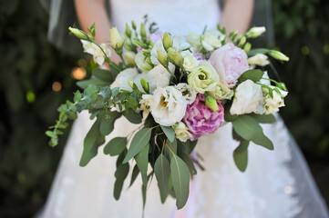 A beautiful large bouquet of colorful fresh flowers with green leaves in the hands of the bride. Wedding photography.