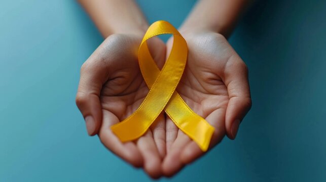Healthcare, charity and medicine concept - close up holding yellow gold childhood cancer awareness ribbon.