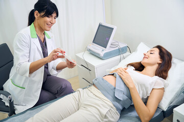 Gynecologist showing to young pregnant woman electrocardiogram of her belly