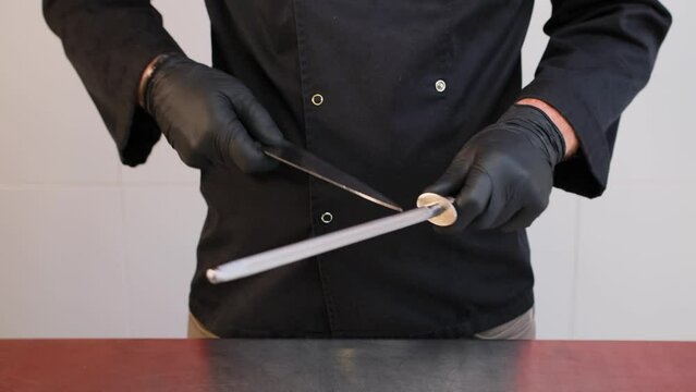 Chef sharpening a knife on an old fashioned handheld a metal file in a close up on his hands