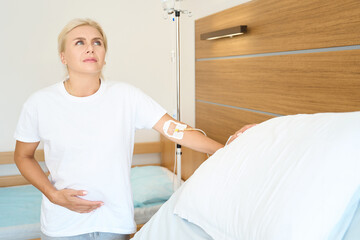 Serious adult european pregnant woman touching her belly in maternity clinic