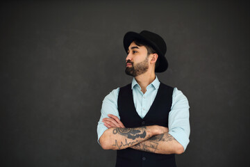 Studio portrait of handsome ethnic male with crossed tattooed arms, dressed in a blue shir