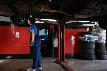 Female in blue uniform stands under the car, raised on lift