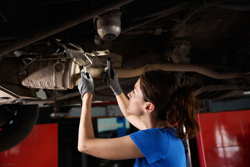 Female auto mechanic inspects the chassis of the car