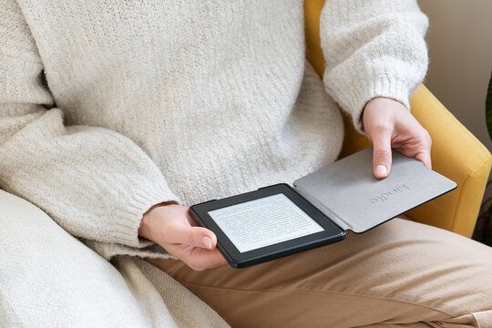A man in a cozy sweater reads an ebook Kindle on a digital tablet, sitting comfortably. The setting is indoors and creates a warm and comfortable atmosphere.
