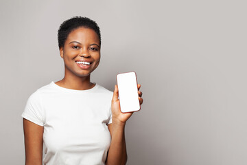 Positive woman showing smartphone with empty blank screen display. Model in white t-shirt with...
