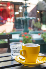espresso coffee in a yellow cup with a glass of sparkling water in a café in the square with fountains