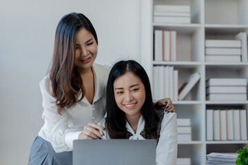 Obraz premium Cheerful business people using a laptop in an office, happy young entrepreneurs smiling while working together in a modern workspace, Two young business people sitting together at a table.