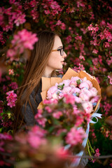 Fototapeta premium Young woman with a bouquet of peonies stands among paradise apple trees