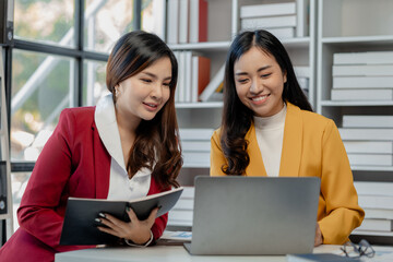 Cheerful business people using a laptop in an office, happy young entrepreneurs smiling while working together in a modern workspace, Two young business people sitting together at a table.