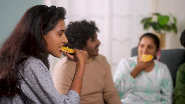Group of friends enjoying eating pizza during weekend gathering at home - concept of socializing, reunion party and togetherness