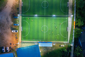 Aerial top view of people playing soccer football sport recreation field ground, national stadium with university or college school campus buildings.Urban city town in Asia. Green court arena at night