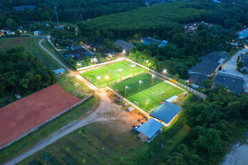 Aerial top view of people playing soccer football sport recreation field ground, national stadium with university or college school campus buildings.Urban city town in Asia. Green court arena at night