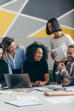 Happy young business team looking at laptop while having group meeting in the office together