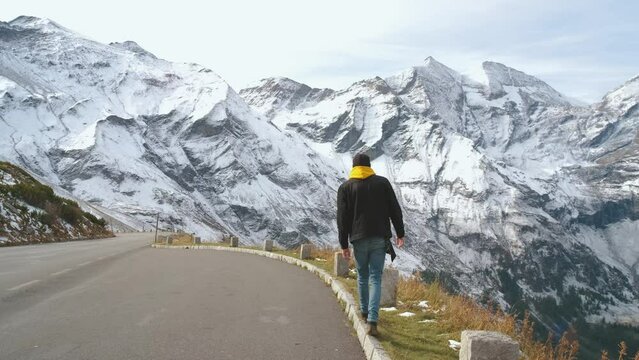 Man traveler walks along Majestic Grossglockner Mountain Road in Austria, snow covered sharp peaks of the alpine mountains on background. Incredibly beautiful views in the Alpine mountains. Route in