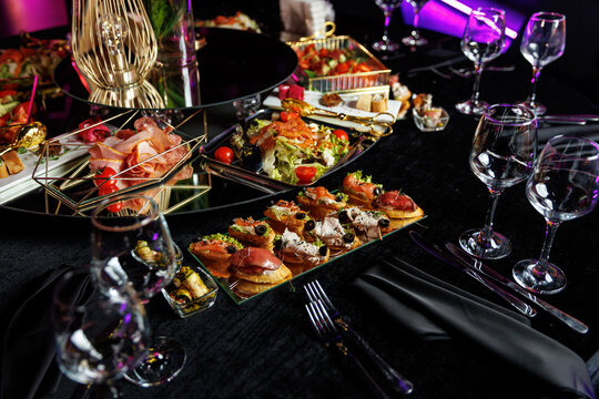 Festive tables with decor on black tablecloth and snacks ready for event.