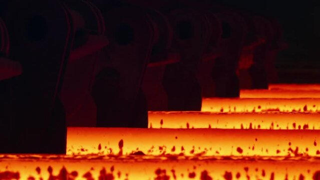 Hot metal sheet slides along the conveyor. Heavy industry. Red hot steel metal billets after molten steel casting. Hot steel bars on the conveyor.