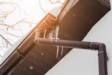Icicles Roof Gutter Problem in Winter. Frozen Ice Dams of Gutter Roof with Frozen Downspout or...