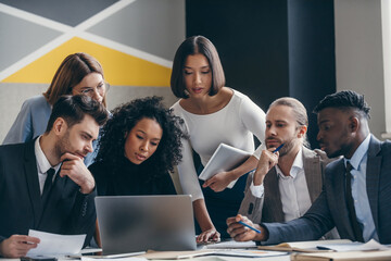 Group of confident young business people looking at laptop while working at the modern office 