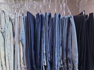 Many jeans are hanging on a rack. Close-up of jeans hanging in the store. Jeans or denim pants hanging on a hanger in a clothing store. The concept of shopping, sales and jeans fashion.