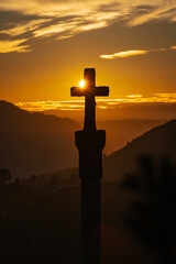 Silhouette one of the numerous medieval cruceiros (calvary) in Ourense against an orange sky.
