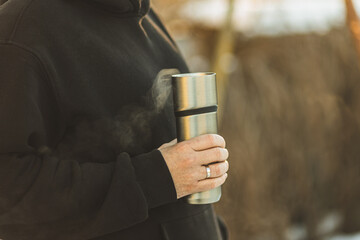 A man holds a thermos mug in his hands. Close-up of thermos in hands. Warming in winter.