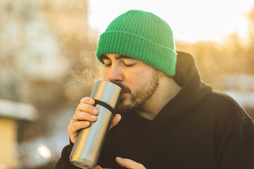 A man holds a thermos mug in his hands. Close-up of thermos in hands. Warming in winter.