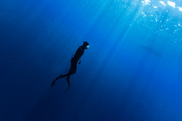 Freediver Swimming in Deep Sea With Sunrays. Young Man DIver Eploring Sea Life.