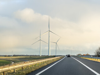 Tall green energy wind mills or turbines near a highway under at sunrise