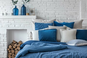Bed with blue pillows and coverlet near fireplace against white brick wall. Loft, Scandinavian interior design of modern bedroom.