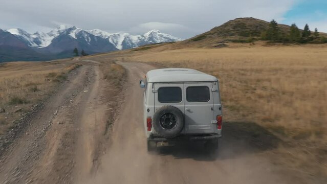 Gray car microbus driving on rural road in mountains valley, rocks, steppes in summer. Picturesque mountains with snowy caps in wild nature. Road car trip, adventure travel tourism vacations concept