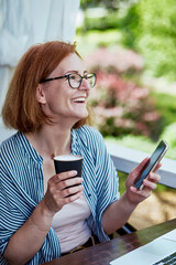 Digital life - cheerful woman browsing on her phone with a drink