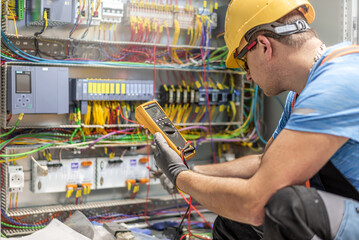 The electrician works with multimeter during connects the wiring in the fuse box. Work in...