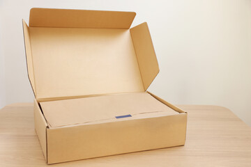 Open cardboard box with item wrapped in kraft paper on wooden table. Delivery service