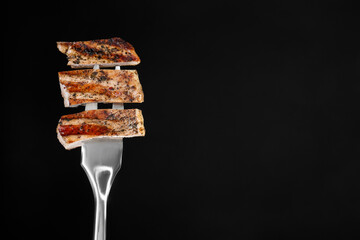 Meat fork with pieces of delicious grilled pork steak against black background, space for text
