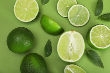 Flat lay composition with fresh limes and leaves on green background