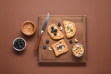 Toasts with tasty nut butter, blueberries, banana slices and cashews on brown table, flat lay
