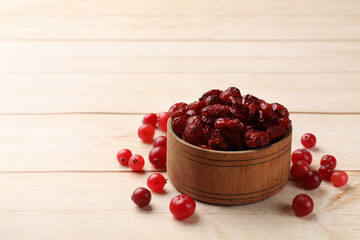 Dried cranberries in bowl and fresh berries on wooden table, space for text