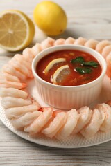 Tasty boiled shrimps with cocktail sauce and lemon on white wooden table, closeup