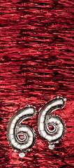 Silver foil balloon number 66 on a background of red tinsel decoration. Birthday greeting card,...